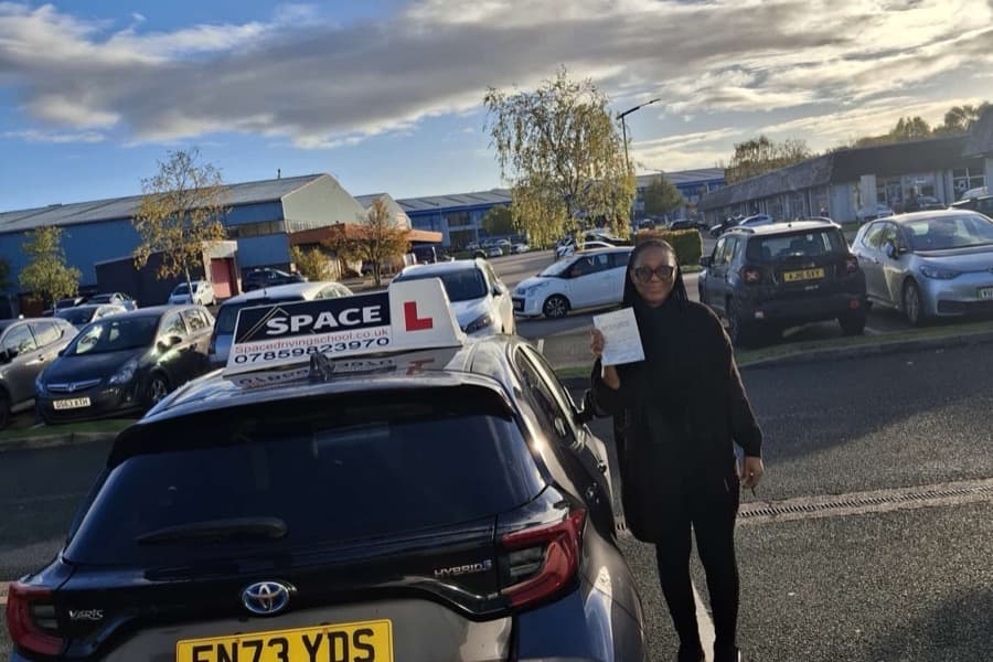 Passed learner holding a driving test certificate beside a Space Driving School car